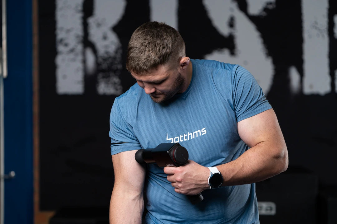 man applying botthms massage gun on his right arm muscle
