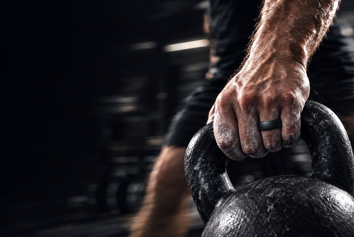 Black botthms silicone ring on a chalked hand holding a kettlebell