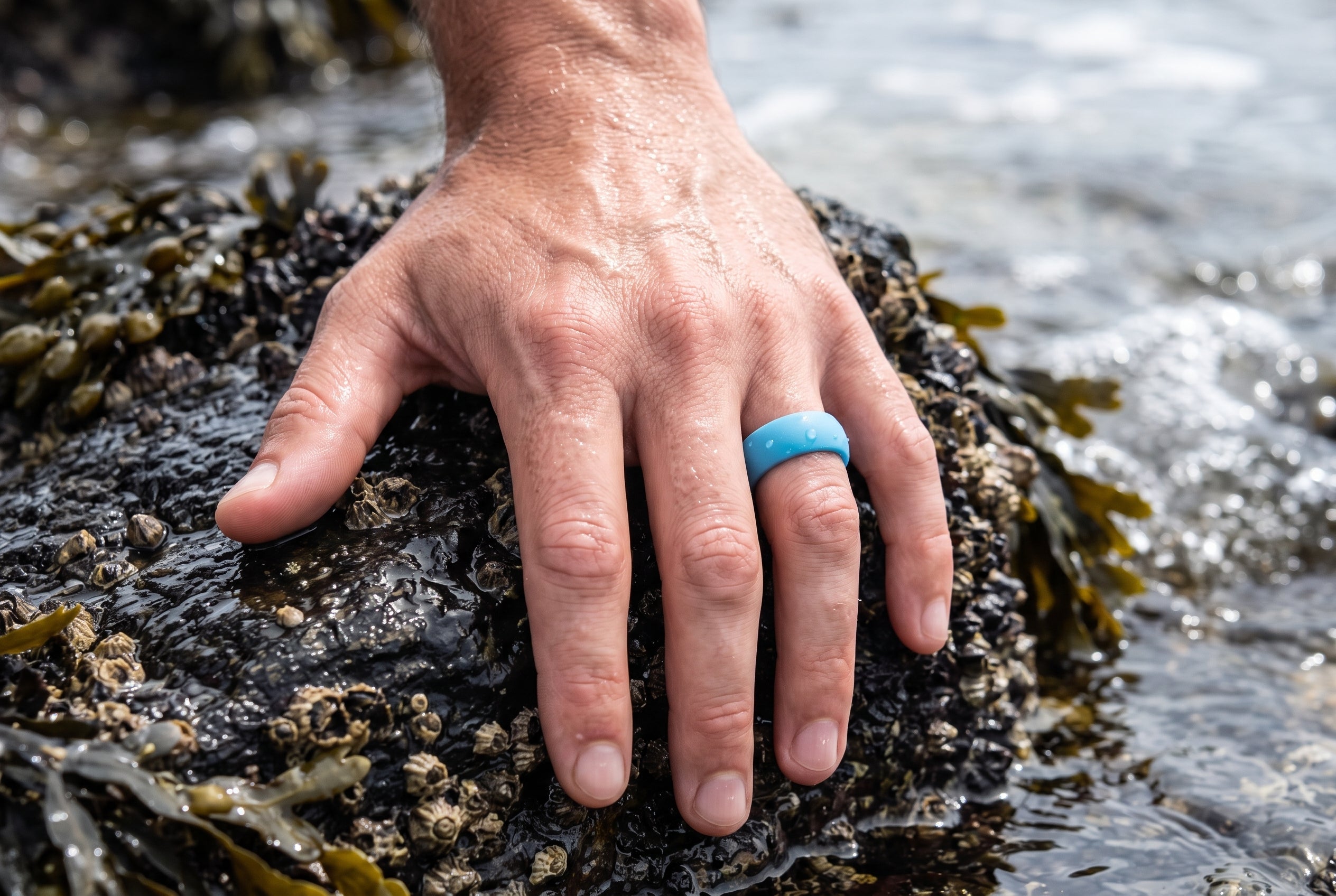Turquoise men's silicone ring worn on a wet hand resting on a rock in a Cornish tidal pool