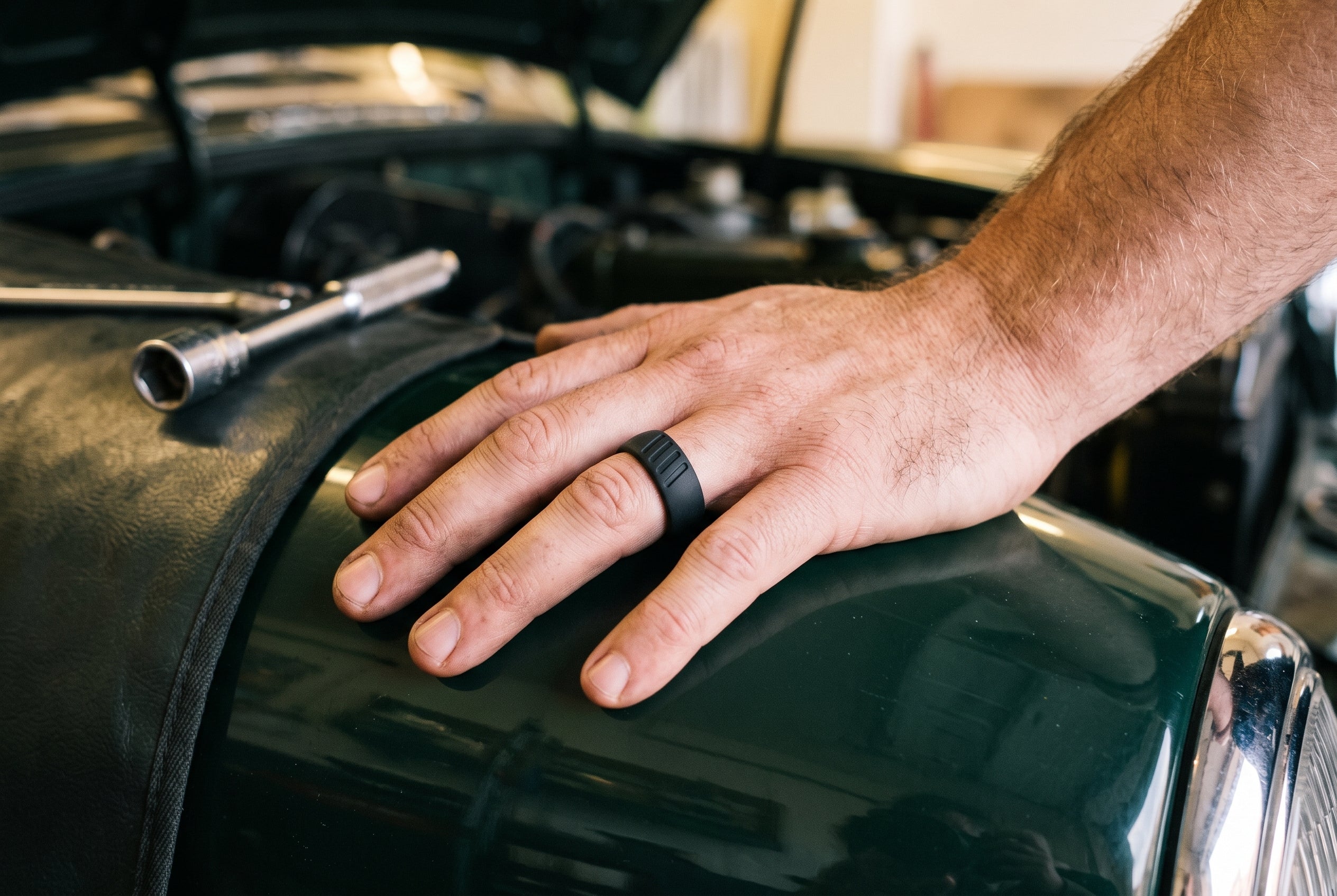 Black men's silicone ring with moulded stripes worn on the wing of a classic car in a home garage