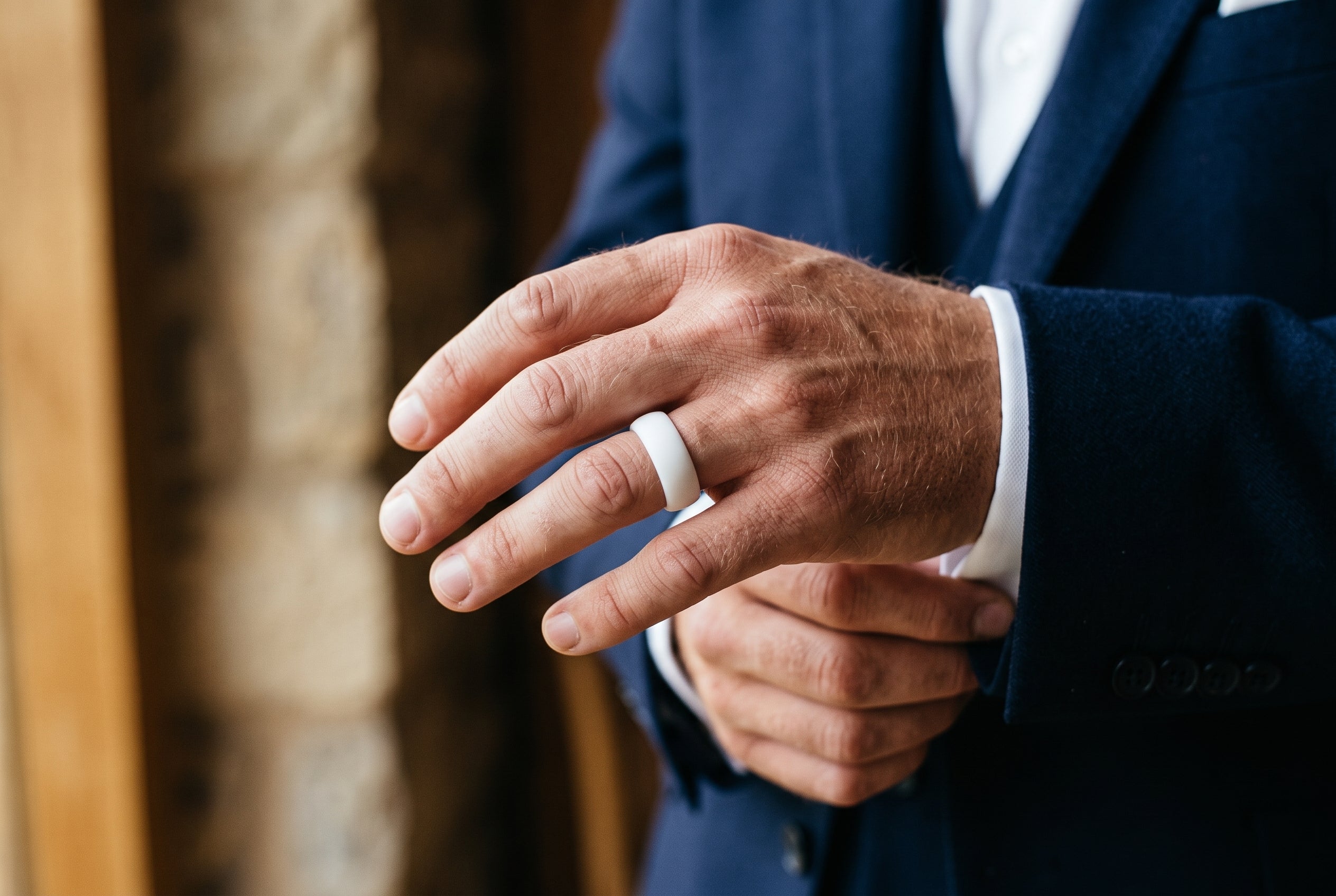 White men's silicone ring worn by a groom adjusting his navy suit cuff at a countryside wedding