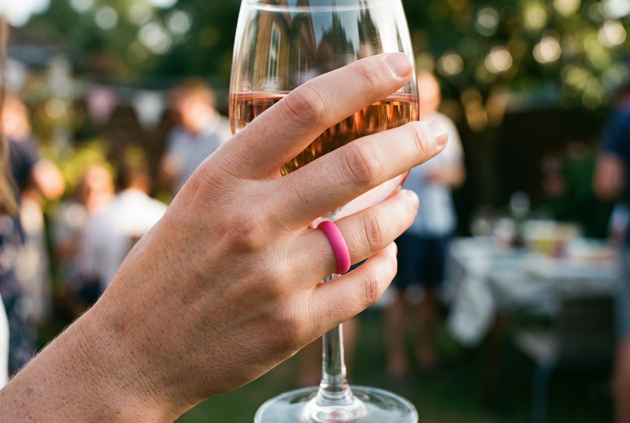 Pink women's silicone ring worn holding a glass of rosé at an English garden party