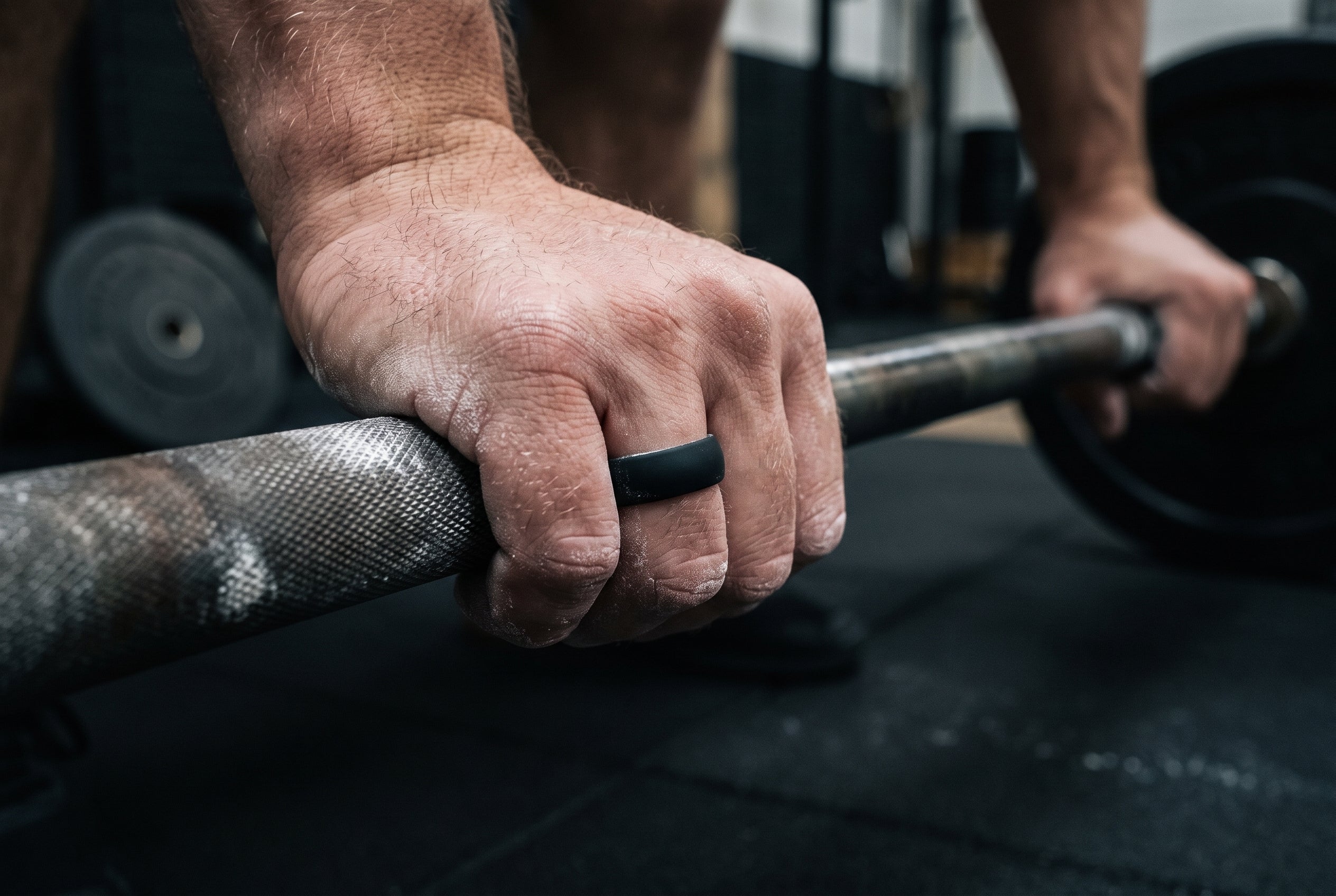 Black men's silicone ring worn on the ring finger while gripping a chalked barbell in a London gym