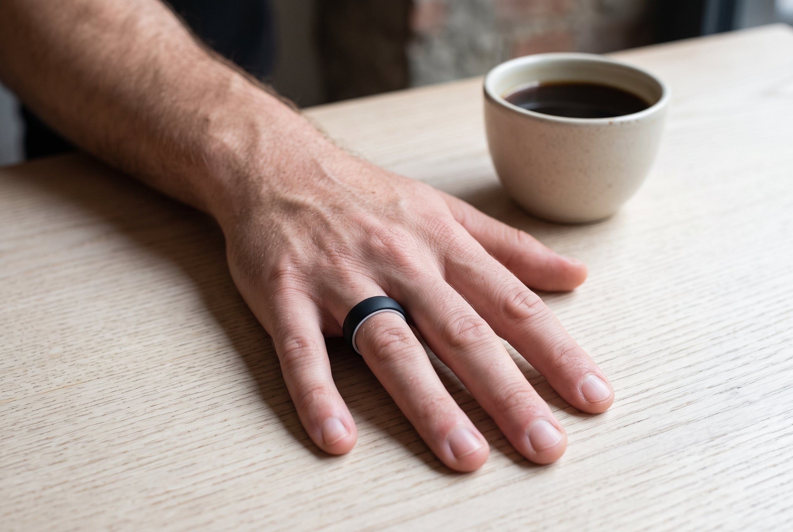 Black men's silicone ring with white inner edge worn beside a black coffee in a Shoreditch café