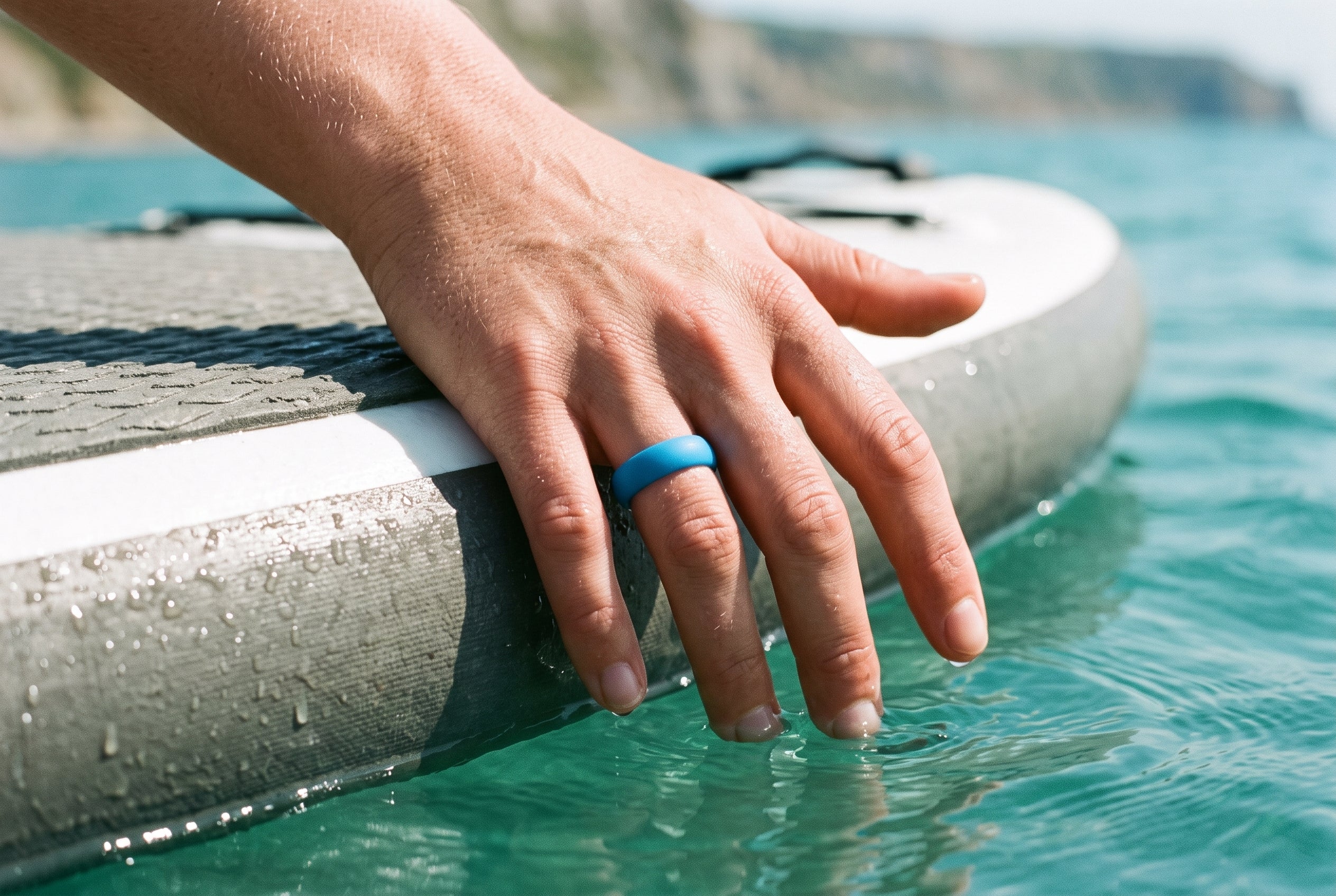 Turquoise women's silicone ring worn with fingertips trailing in the sea from a paddleboard on the Dorset coast