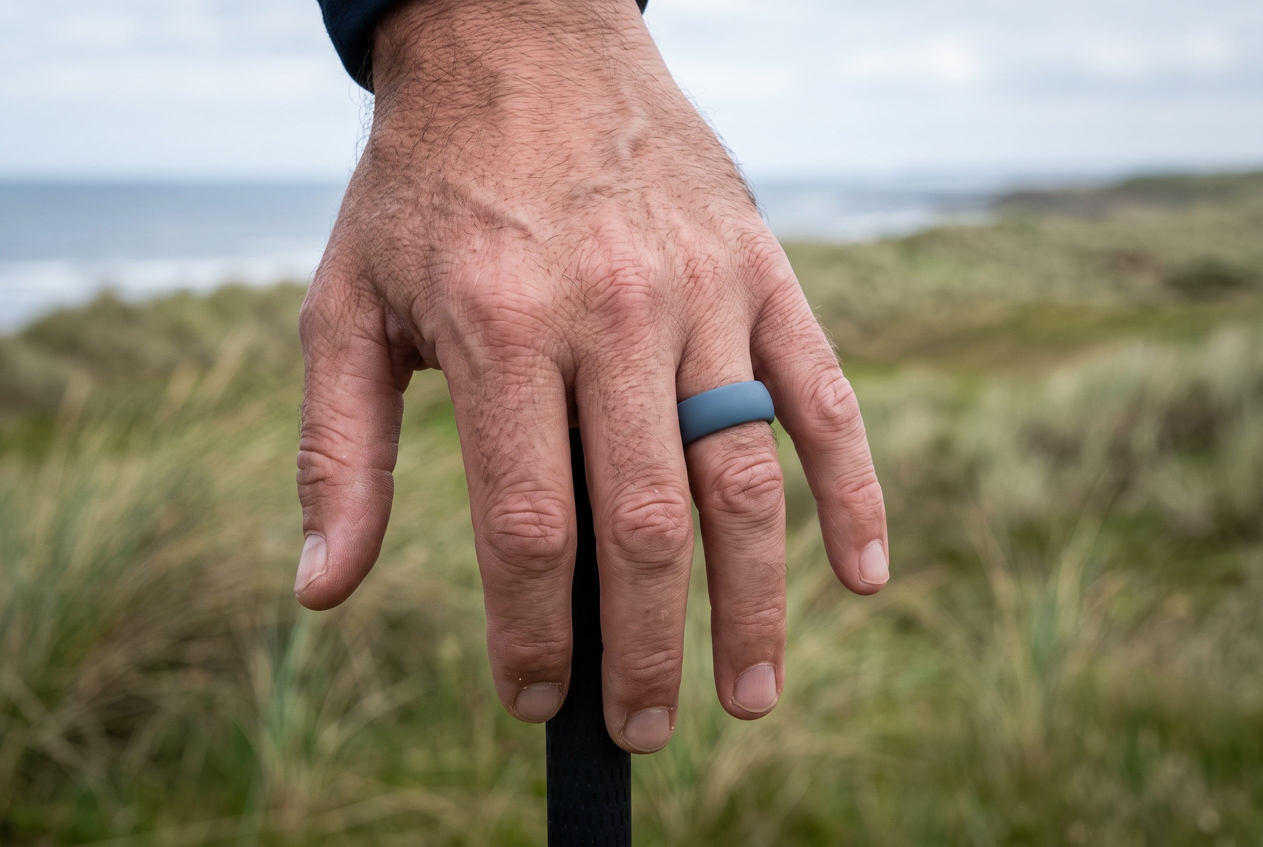 Teal blue men's silicone ring worn with a hand resting on a golf club at a Scottish links course