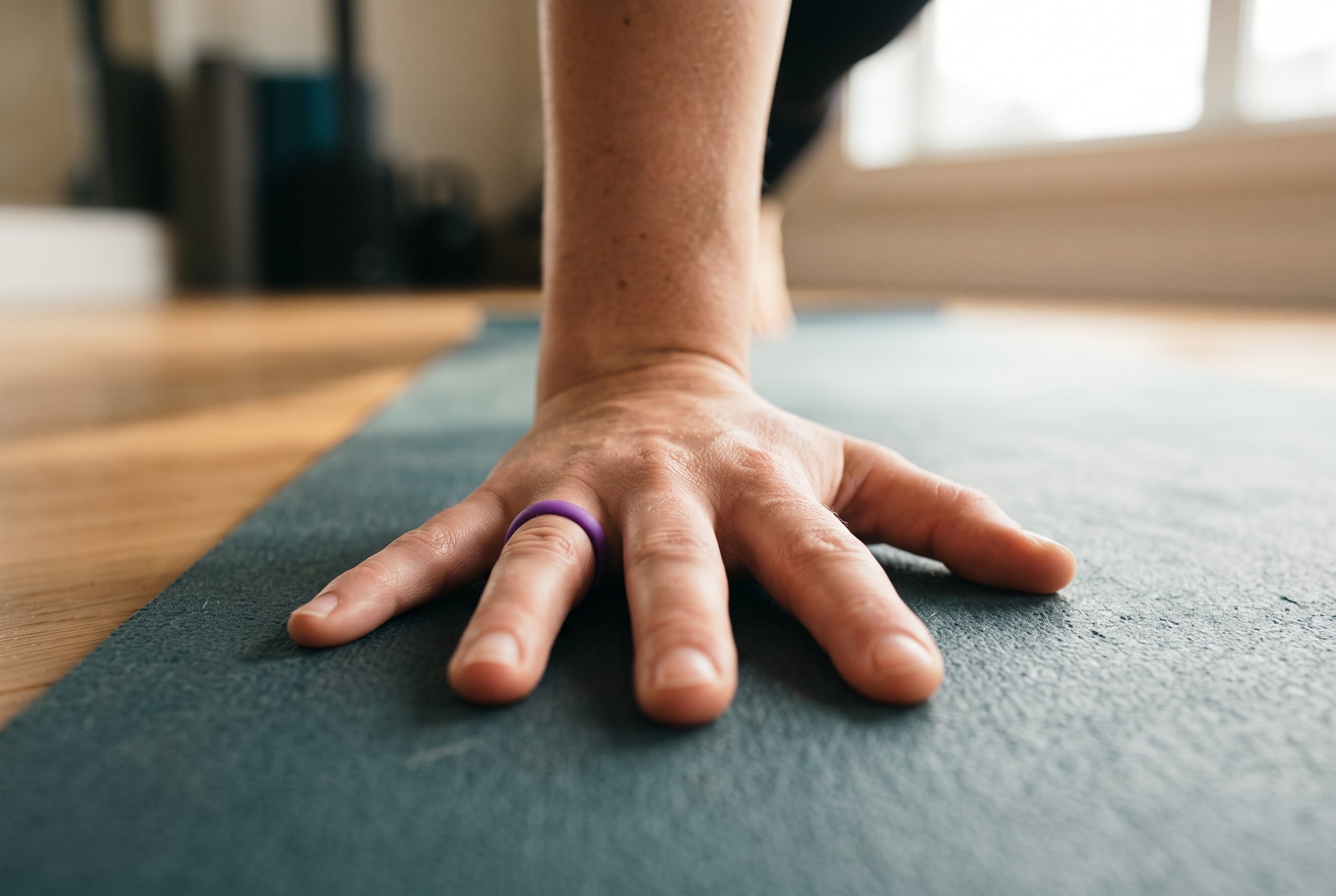 Purple women's silicone ring worn with the hand pressed flat on a yoga mat in a sunlit studio