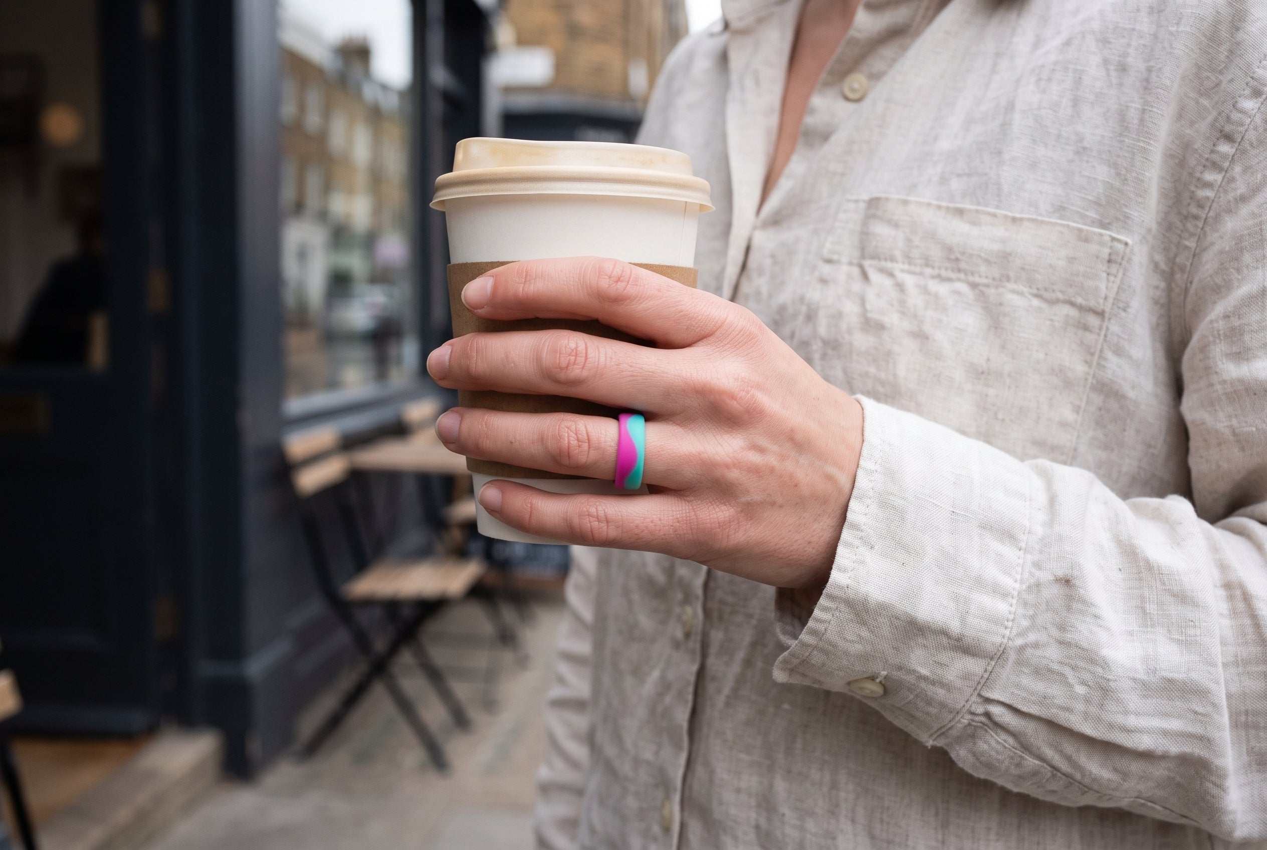 Pink and turquoise Flow women's silicone ring worn while holding a takeaway flat white outside a London café