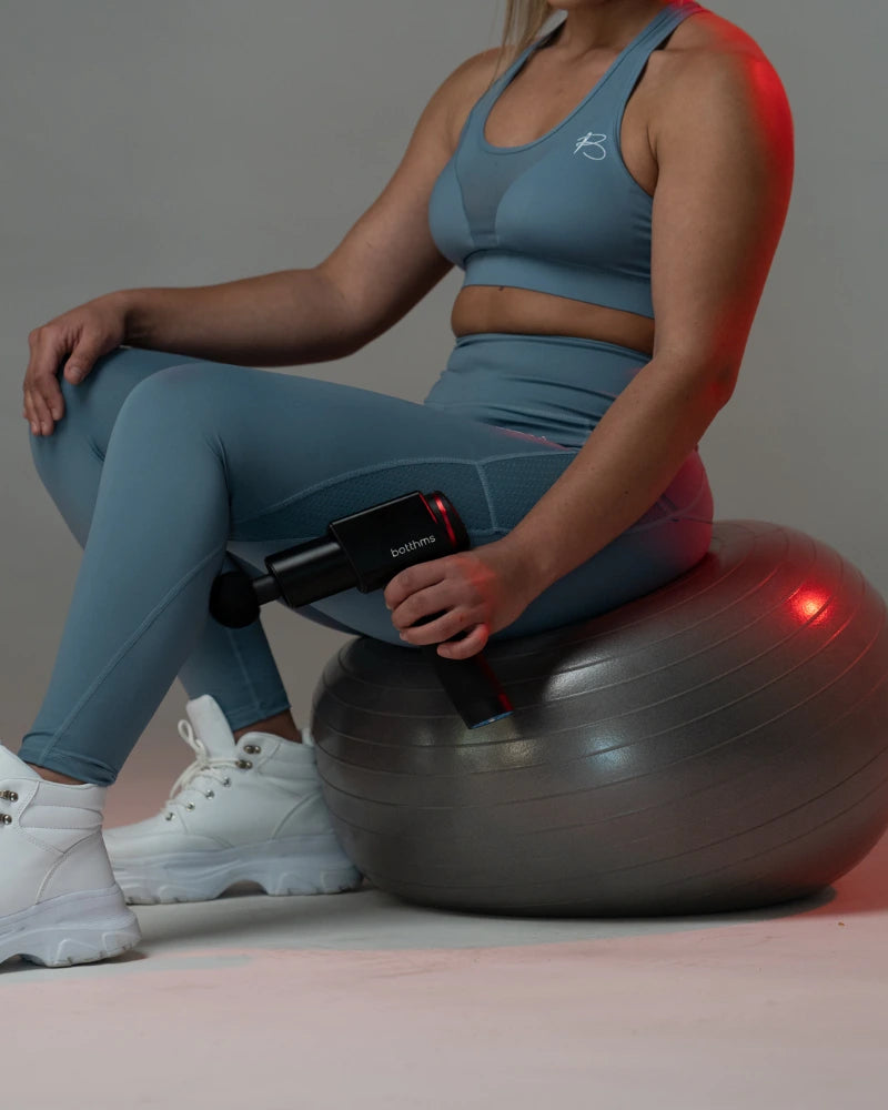 young blonde trying botthms massage gun on her left leg lower part muscle