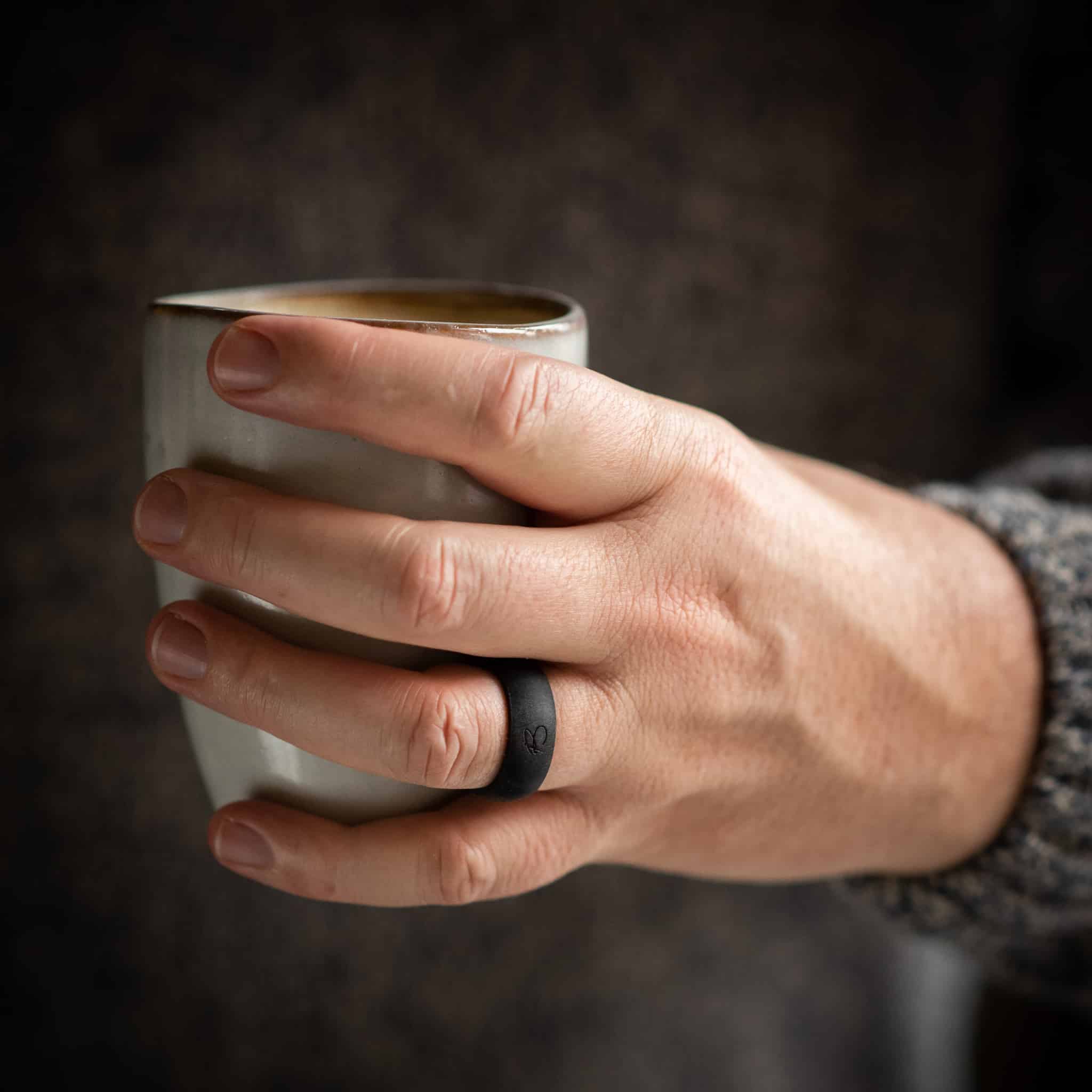 a hand holding a tea cup and wearing botthms black active silicone ring